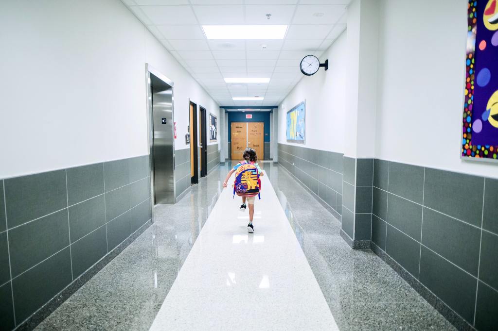 Small child with backpack on, running through an empty school hallway.